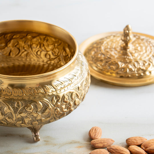 Brass handi crafted with embossed floral detailing and a matching lid designed with a decorative top handle and round legs