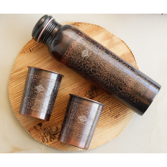 Antique copper water bottle with embossed floral design, paired with matching glasses in a softly lit home environment.