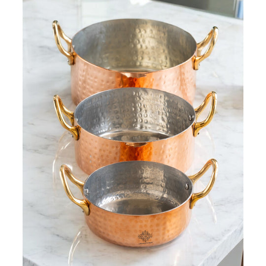 Beautifully crafted hammered copper cookware with brass handles, arranged in descending order.