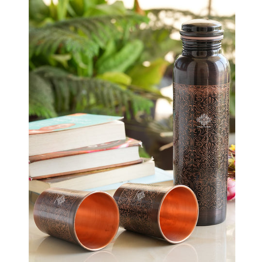 Antique copper water bottle with embossed floral design, paired with matching glasses in a softly lit home environment.
