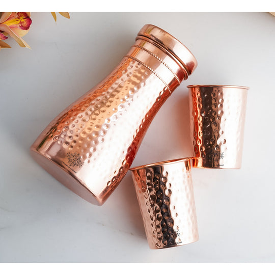 Luxurious hammered copper drinkware set, featuring a bottle and tumblers, perfect for décor and daily use.