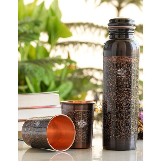 Antique copper water bottle with embossed floral design, paired with matching glasses in a softly lit home environment.