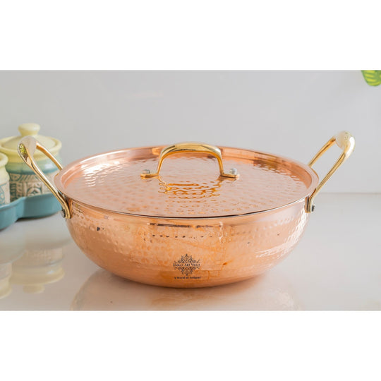 Handcrafted copper kadhai with brass handles and lid featuring a hammered design and tin lining for cooking versatility
