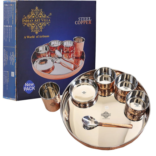 A set of copper hammered design dinnerware, including a thali (plate), katoris (bowls), a glass, and a spoon, displayed on a white surface.