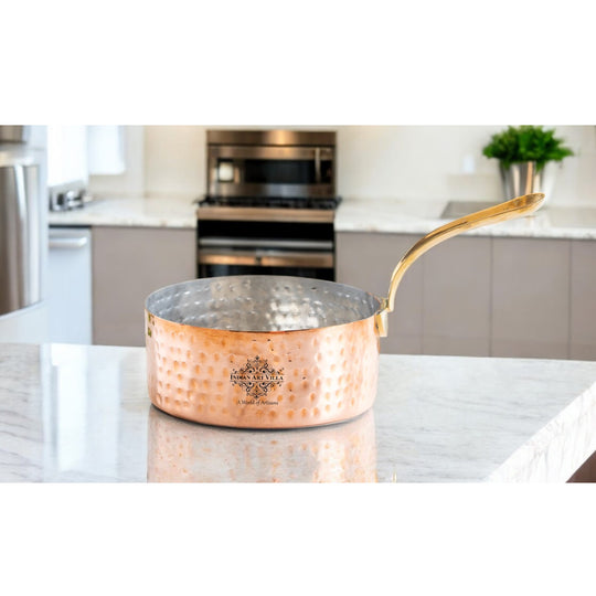 Handcrafted copper saucepan with a smooth, hammered texture and elegant brass handle, perfect for cooking.