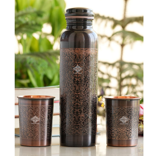 Antique copper water bottle with embossed floral design, paired with matching glasses in a softly lit home environment.
