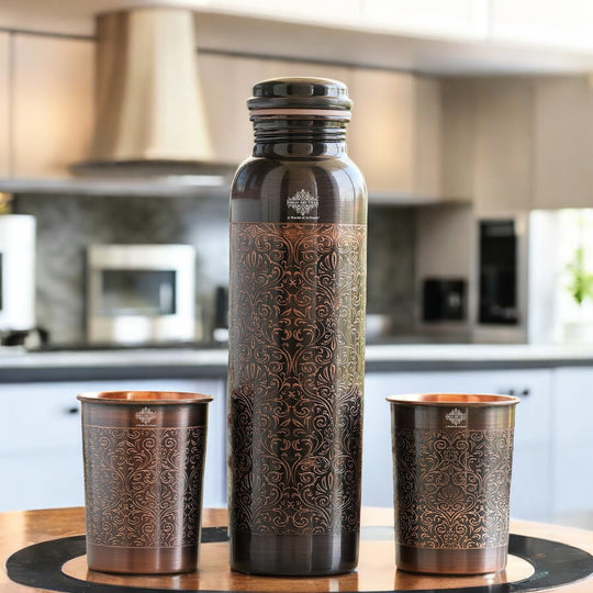 Antique copper water bottle with embossed floral design, paired with matching glasses in a softly lit home environment.