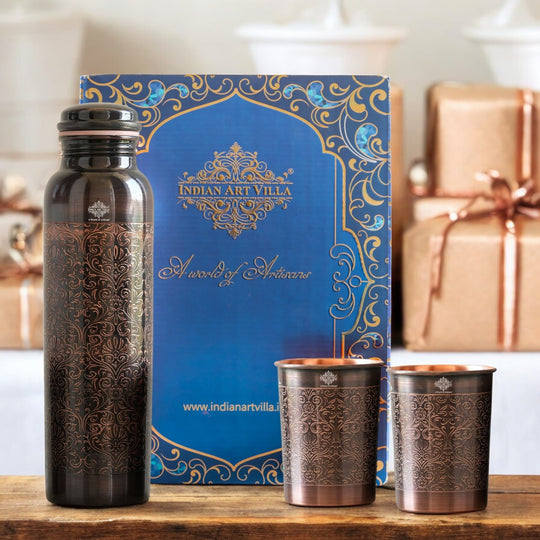 Antique copper water bottle with embossed floral design, paired with matching glasses in a softly lit home environment.