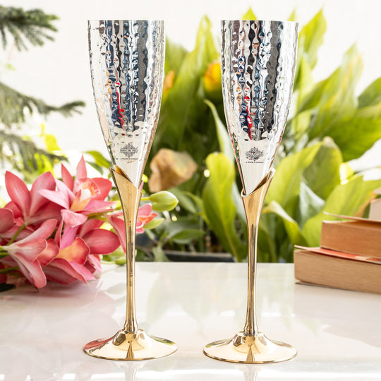Two silver and gold champagne flutes on a table with flowers and a box in the background.