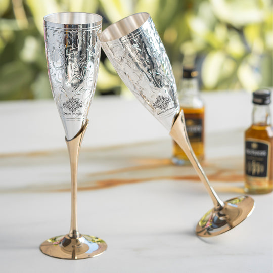 Two silver champagne flutes with gold bases on a blurred background