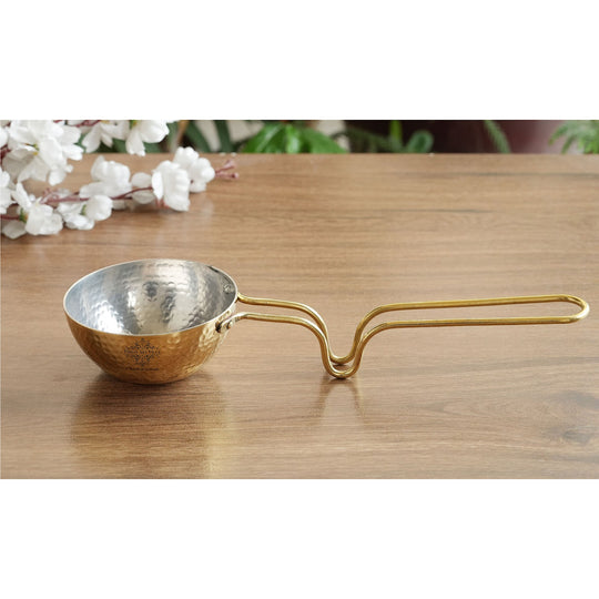 Handcrafted brass tadka pan with polished finish tin coated interior and extended handle commonly used for Indian tadka